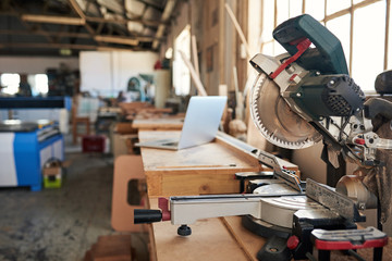 Mitre saw and laptop on workbenches in a woodworking shop