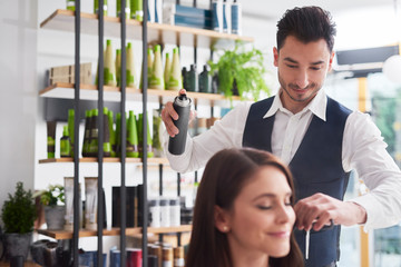 Male hairdresser using hairspray at work