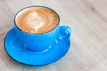 defocused blue cup of latte coffee on a light wooden background