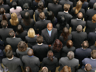 Black businessman looking at the camera standing in the middle of a large crowd that is looking away