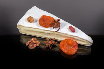Brie cheese, nuts, dried fruits on a dark reflective surface