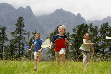 Three young children running through a field chasing each other whilst having fun