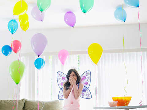 Young Girl (7-9) With Fairy Wings In Room Full Of Balloons