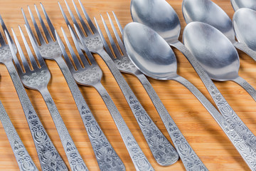 Spoons and forks laid on wooden surface, fragment close-up