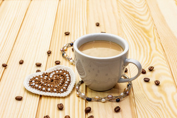 Valentine's Day concept. Cup of coffee, knitted heart, string of pearl beads. Romantic breakfast and gift on wooden boards background