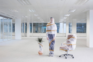 Office worker swivel chair and potted plant covered with bubble wrap and tape in empty office space