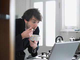 Man eating breakfast cereal while looking at laptop screen