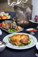 Baked full chicken with vegetables in a plate on a table next to glass of wine and candles. Outdoor, green park