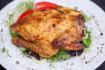 fried full chicken with vegetables and herbs in a plate on the table