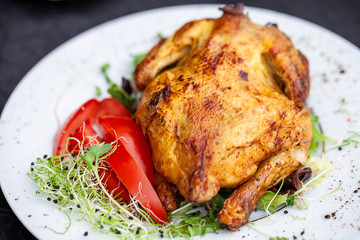 fried full chicken with vegetables and herbs in a plate on the table