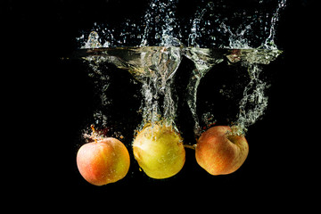 Fototapeta na wymiar Three apples splashing into water on black background.