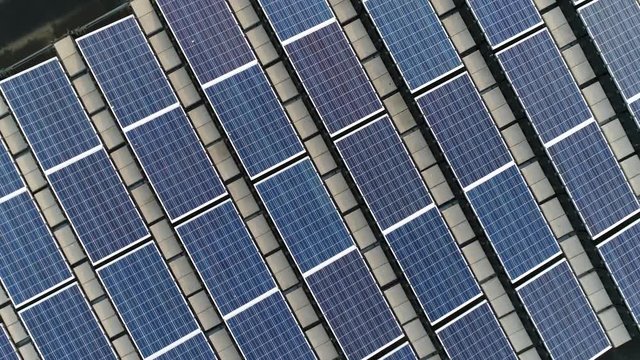 Aerial top down view moving up above solar panels PV modules mounted on flat roof photovoltaic these absorb sunlight as a source of power to generate electricity creating sustainable energy 4k quality