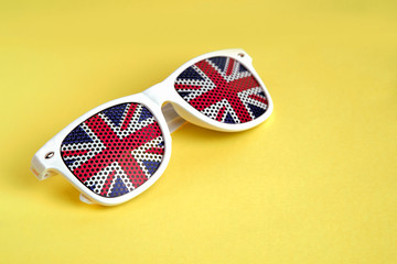 White rimmed sunglasses with UK flag on a yellow isolated background. Selective focus. Free space for your text.