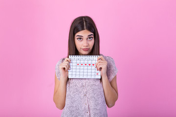 Portrait of disappointed outraged woman 20s holding period calendar isolated over pink background in studio. Beautiful young woman standing isolated over pink background, showing menstrual calendar