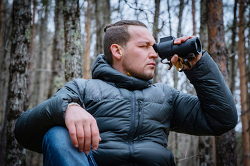Traveler with monocle sitting on big stone in deep forest and looks into the distance.