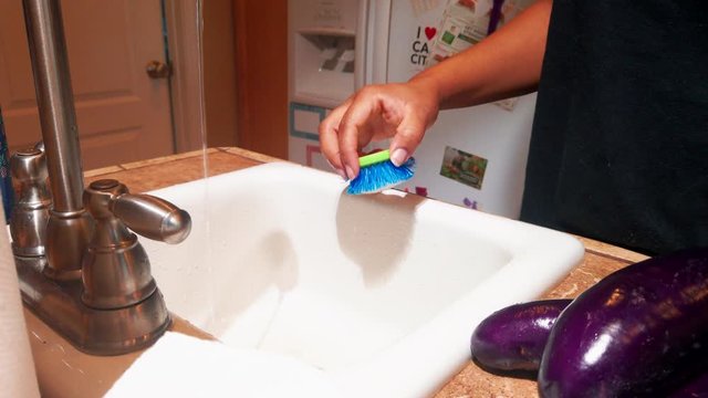 A woman cleaning a zucchini with a brush under running water - Close up
