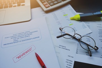 The reviewed financial statement, eyeglass, highlight pencil, calculator, laptop and edited paper. It's important work of the account, finance, internal and external audit must to accurate and timely