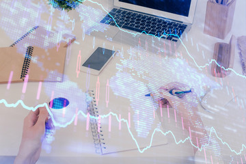 Hands writing information about stock market in notepad. Forex chart holograms in front. Concept of...