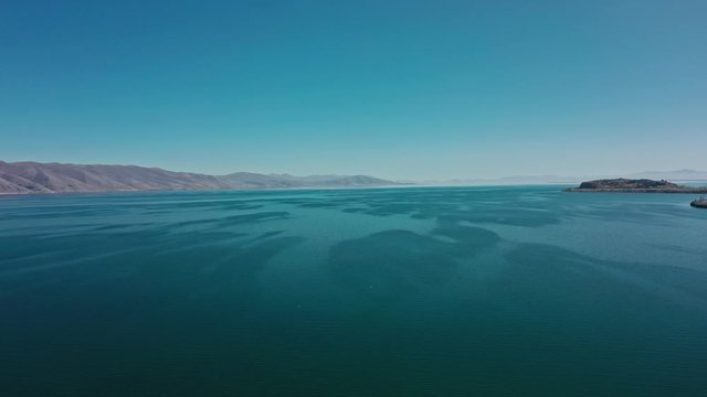 Aerial drone pan shot right to left of Lake Sevan on background of Mount Ararat. Aerial drone zoom in shot of Lake Sevan under bright blue sky