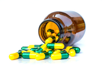 Many yellow-green capsules are pouring out of the bottle. Isolated on white background.