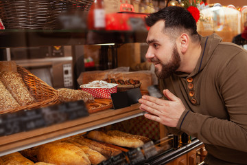Excited man shopping for pastry at local bakery, looking at the showcase