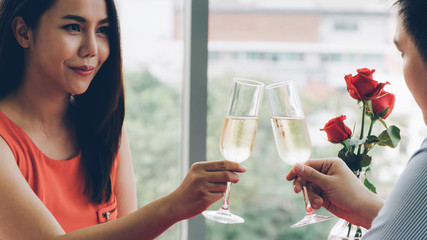 Asian young couple hand holding glasses of champagne having romantic dinner at restaurant, woman smile with love to her boyfriend, dating on Valentine, birthday or anniversary concept