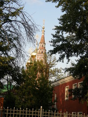 High bell tower and Golden domes of the Cathedral in the distance behind green bushes and a low red building
