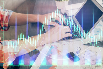Double exposure of stock graph with businessman typing on computer in office on background. Concept of hard work.