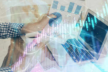 Double exposure of stock graph with businessman typing on computer in office on background. Concept of hard work.
