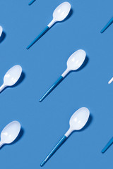 Pattern of white plastic spoons on blue background. Vertical picture. Flat lay, top view.