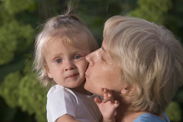 Fototapeta na wymiar Grandmother presses a kiss onto toddler's cheek