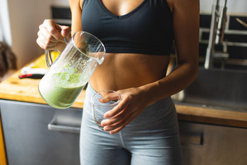 Fitness diet concept. Sporty woman drinking a green detox smoothie for breakfast in the kitchen. - obrazy, fototapety, plakaty
