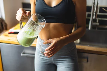 Deurstickers Fitness diet concept. Sporty woman drinking a green detox smoothie for breakfast in the kitchen. © Dirima