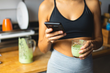 Fitness diet concept. Sporty woman holding a green detox smoothie and using nutrition app on...