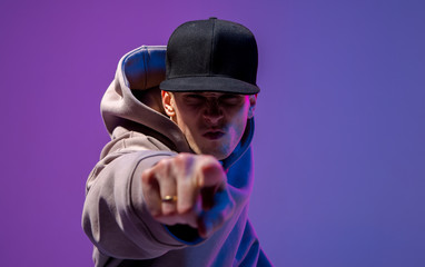 Men portrait in a neon light. Beneath in the hoodie and hat. Dark face. Hip-hop style.