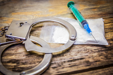 Handcuffs, syringe, bag of drugs on a wooden background close-up