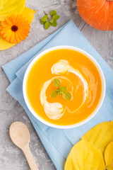 Traditional pumpkin cream soup with in white bowl on a gray concrete background with blue napkin. top view, close up.
