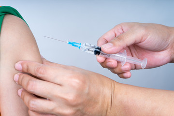 Syringe with needle facing towards boy arm for injection. 