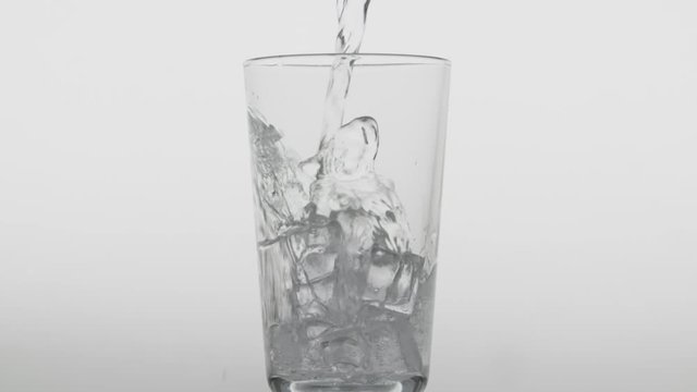 Pouring transparent fizzy drink. Glass full of cold sparkling water with lce cubes on clean white background, moving bubbles in soda slow motion