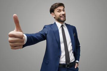 wide angle selfie shot of young business man going thumb up on grey background