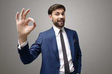 wide angle selfie shot of young business man showing ok sign on grey background