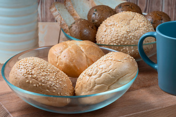 wheat buns with sesame filling in a glass bowl, a ceramic mug and a bottle of milk on the kitchen table.