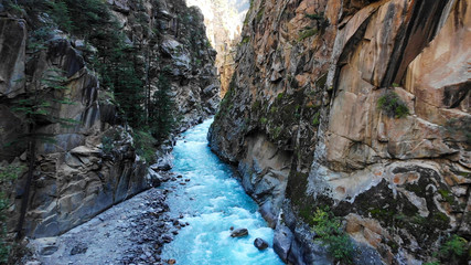 Drone view of a cyrstal clear blue stream of water passing through a narrow valley