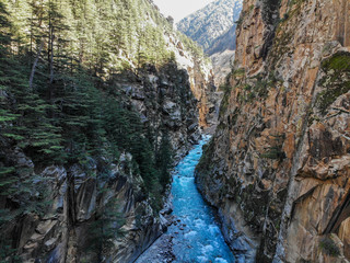 Drone view of a cyrstal clear blue stream of water passing through a narrow valley