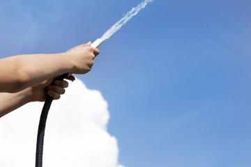 watering hose in the hands of a gardener splashes out a stream of water against a blue sky....