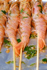 Langoustines on skewers lie on a plate with foil for cooking in the oven