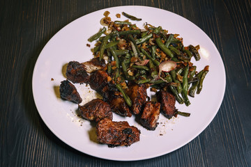 Plate with burnt overcooked meat and garnish on dark background