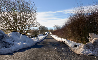 A remote rural road cleared of snow by a snow plough on a bright winters day keeping access open to local communities.