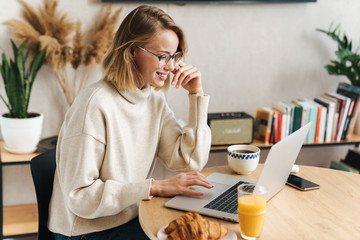 Photo of caucasian woman using laptop while having breakfast at home