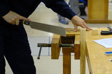 A carpenter cuts a piece of a bar with a hacksaw on a wooden workbench